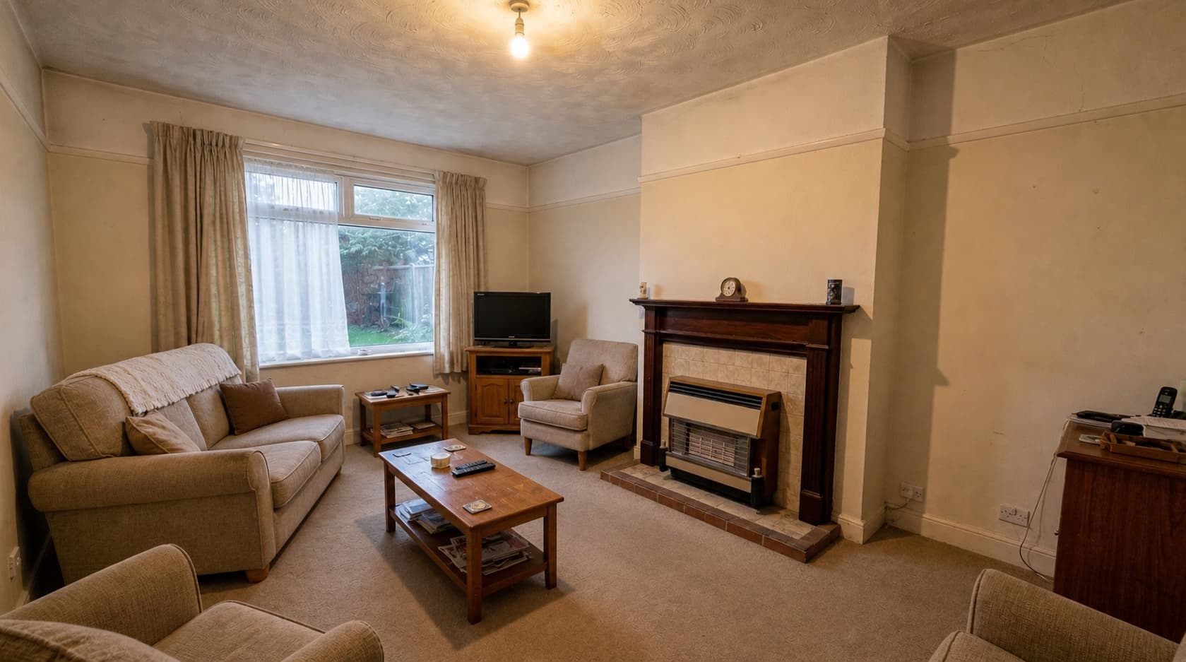 A dated living room with patterned carpet and floral wallpaper, before renovation